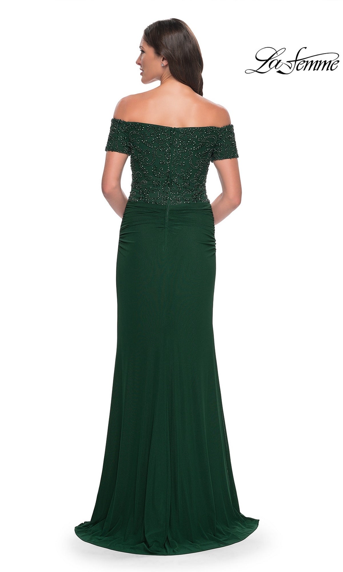 A woman in the Long Formal Dress: La Femme 30057, featuring an off-the-shoulder beaded bodice and floor-length dark green skirt, stands with her back to the camera.